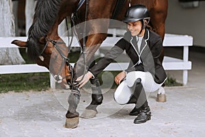 Horse rider preparing bridle at stable. Young beautiful girl preparing her horse before riding. People and equestrianism concept