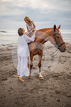 Horse riding on the beach. Cute little girl on a brown horse. Her mom standing near by. Love to animals. Mom and daughter spending