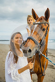 Horse riding on the beach. Cute little girl on a horse. Her mom standing near by. Portrait of woman and brown horse. Love to