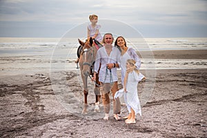 Horse riding. Little pretty girl on a horse. Father leading horse by its rein. Mother hugging daughter. Family concept. Summer