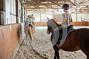 Horse riding school. Little children girls at group training equestrian lessons in indoor ranch horse riding hall. Cute