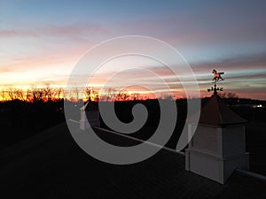 Horse weathervane on the cupola and the silhouette of trees against the orange-red sky at the sunset