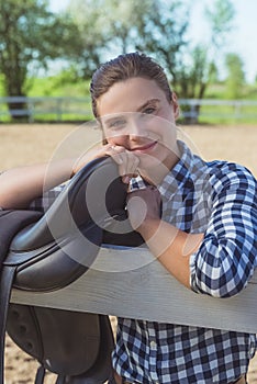 Horse Woman Standing With A Black Leather Saddle Hanging On The Wooden Fence