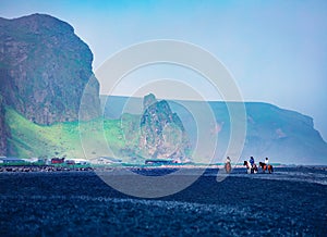 Horseback riding on the famous Black Sand Beach in Vik village. Amazing summer scene of Icelan, Europe.