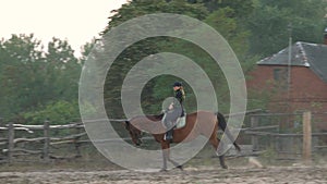 Horsegirl rides gallop on a brown horse in the outdoors sand arena. Competitive rider training dressage in manege