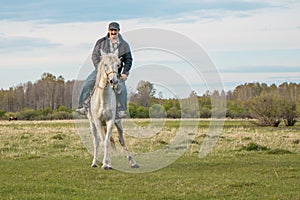Horseman on a white horse rides through the pasture