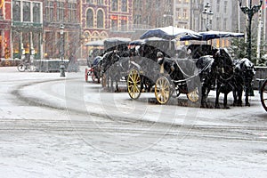 Horses carriage with old fashioned coach under snowfall on empty square in Europe. Winter travel background.