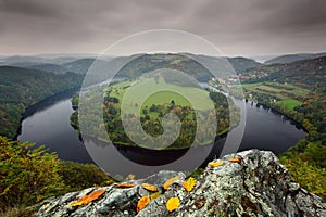 Horseshoe bend, Vltava river, dark clouds with autumn leaves on the rock, Solenice, Czech republic