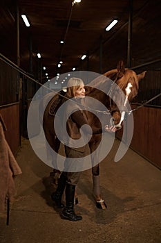 Horsewoman petting horse stroking animal muzzle over stable interior