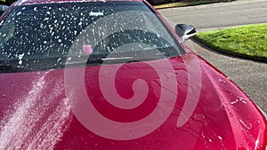 Hose with nozzle spraying water on soapy car