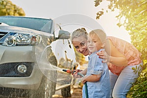 Hosing down the car together. Portrait of a mother and son washing a car together.