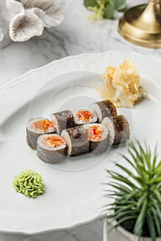 Hosomaki salmon sushi roll with chili sauce in the white plate on light marble background. Healthy sea food, hard light,