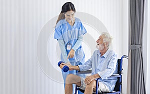 Hospice nurse is helping Caucasian man in wheelchair to exercising muscle strength in pension retirement center for home care
