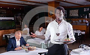 Hospitable african american waiter greeting guests in restaurant