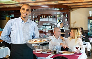 Hospitable latin american waiter welcoming guests in pizza restaurant