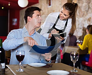 Hospitable waitress helping handsome man with menu, taking order in restaurant