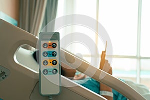 Hospital bed remote control hanging on the bed rail with woman patient on bed in hospital room