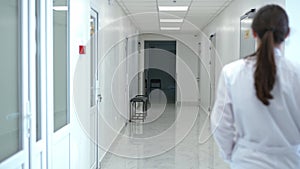 Hospital corridor with young woman in uniform entering walking indoors. Caucasian professional confident doctor