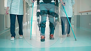 Hospital hall with a man walking in the exoskeleton with assistance