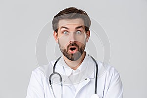 Hospital, healthcare workers, covid-19 treatment concept. Close-up of surprised, amazed bearded doctor in white scrubs