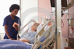 Hospital Nurse With Digital Tablet Talks To Senior Patient