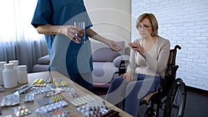 Hospital nurse giving pills to female patient in wheelchair treatment routine