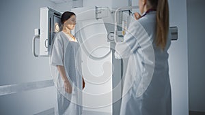 Hospital Radiology Room: Beautiful Multiethnic Woman in Medical Gown Standing Next to X-Ray Machin