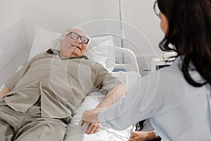 In the hospital room laying down on the bed old man focus on hands he is recover and resting while his daughter holding