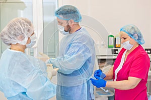 Hospital. Surgeon operates in the operating room. Profile view of a medical assistant helping a surgeon put on his