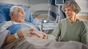 Hospital Ward: Elderly Man Resting in Bed, His Caring Beautiful Wife Supports Him Sitting Beside,