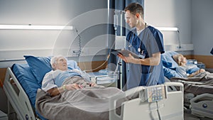 Hospital Ward: Friendly Male Nurse Talks with Elderly Patient Resting in Bed. Doctor Uses Tablet C