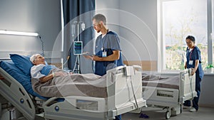 Hospital Ward: Friendly Male Nurse Talks Reassuringly to Elderly Patient Resting in Bed. Doctor or