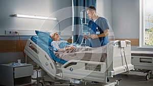 Hospital Ward: Friendly Male Nurse Talks to Beautiful Female Patient Resting in Bed. Male Nurse or