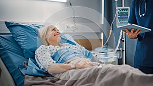 Hospital Ward: Friendly Male Nurse Talks to Beautiful Female Patient Resting in Bed. Male Nurse or