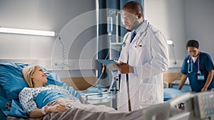 Hospital Ward: Handsome Black Doctor Wearing Glasses Uses Digital Tablet Computer, Checking Patien