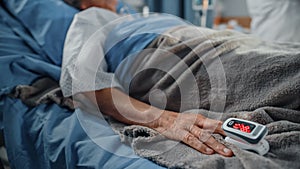 Hospital Ward: Senior Woman Resting in a bed with Finger Heart Rate Monitor / Pulse oximeter showing