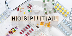 HOSPITAL word on wooden blocks on a desk. Medical concept with pills, vitamins, stethoscope and syringe on the background