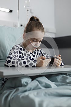 Hospitalized ill kid watching cartoons on phone while sitting inside pediatric healthcare clinic ward