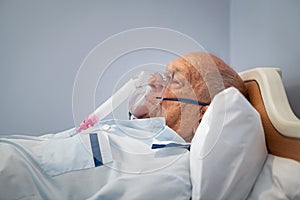 Hospitalized senior patient lying on bed with oxygen mask at hospital