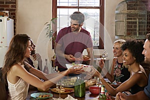 Host and friends pass food round the table at a dinner party