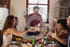 Host and friends pass food round the table at a dinner party