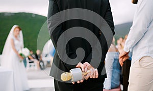 The host at a wedding party stands and holds a microphone behind his back, close-up