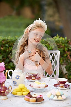 Hosting a pretend tea party. A cute little girl having a tea party outside.