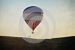 A hot air balloon floating above a couple on a summers evening. With a grunge, artistic edit