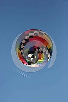 A hot air balloon floats overhead as an airplane leaves a vapor trail at a higher altitude