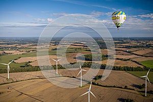 Hot air balloon flying over wind turbines on a farm field.