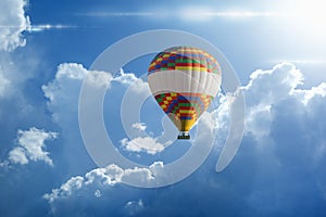 Hot air balloon rises very high in blue sky above white clouds