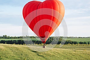 Hot air balloon in shape of heart is landing on the green field