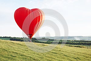 Hot air balloon in the shape of a heart is landing on the green valley