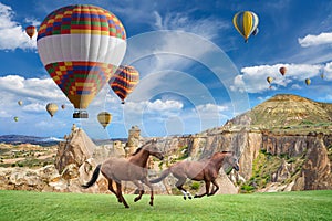 Hot air ballooning and two horses running in Cappadocia, Turkey.